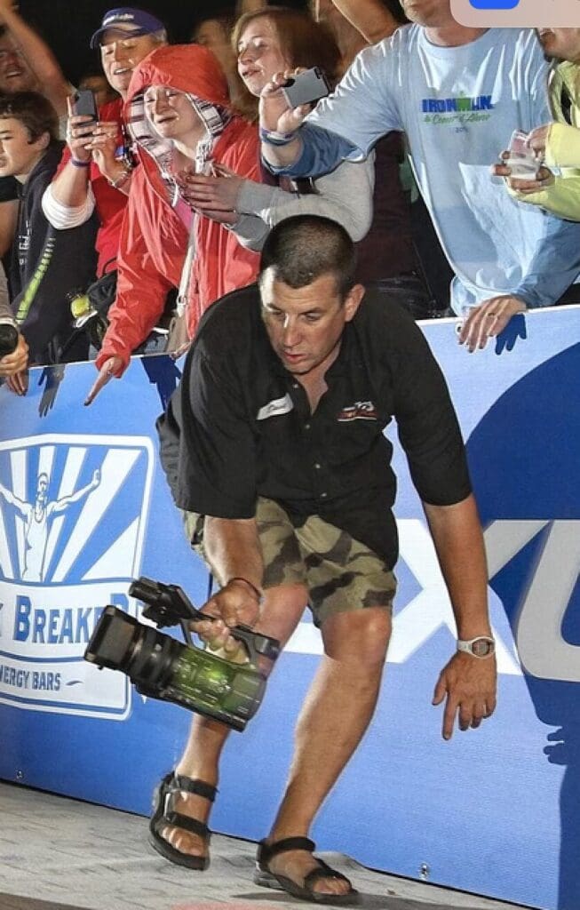 Dave filming an athlete finishing while wearing his name shirt.